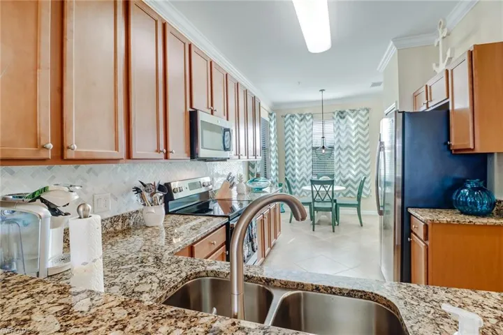 Kitchen with appliances with stainless steel finishes, light stone countertops, crown molding, tasteful backsplash, and light tile patterned floors