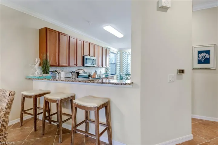 Kitchen with appliances with stainless steel finishes, ornamental molding, light tile patterned flooring, a breakfast bar area, and brown cabinets