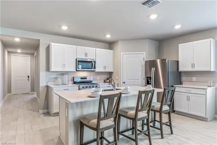 Kitchen with a kitchen breakfast bar, light wood-style flooring, appliances with stainless steel finishes, recessed lighting, and a kitchen island with sink