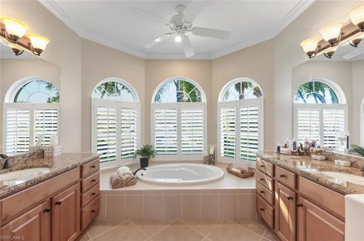 Full bathroom featuring light tile patterned floors, a bath, two vanities, crown molding, and ceiling fan