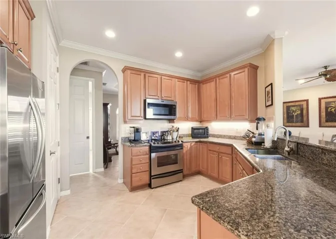 Kitchen with appliances with stainless steel finishes, ornamental molding, dark stone counters, arched walkways, and light tile patterned floors