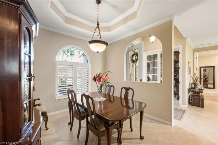 Dining area with crown molding, light tile patterned flooring, a raised ceiling, and arched walkways