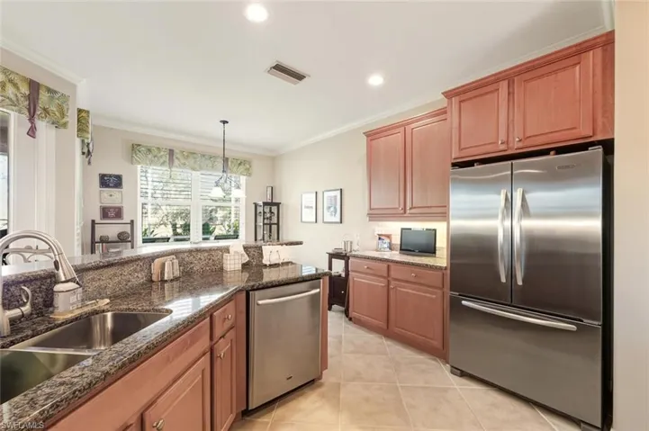 Kitchen with appliances with stainless steel finishes, dark stone counters, ornamental molding, brown cabinets, and pendant lighting