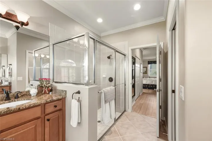 Ensuite bathroom featuring crown molding, vanity, a shower stall, light tile patterned floors, and recessed lighting