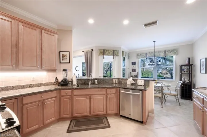 Kitchen with a chandelier, a peninsula, stainless steel dishwasher, dark stone countertops, and crown molding