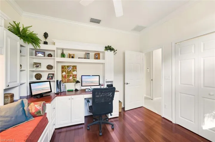 Office with dark wood-style flooring, crown molding, and built in desk