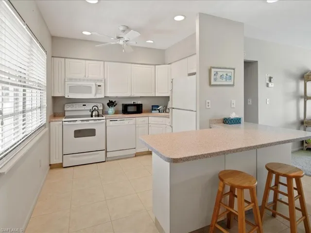 Kitchen with a breakfast bar, light countertops, light tile patterned floors, white cabinets, and white appliances