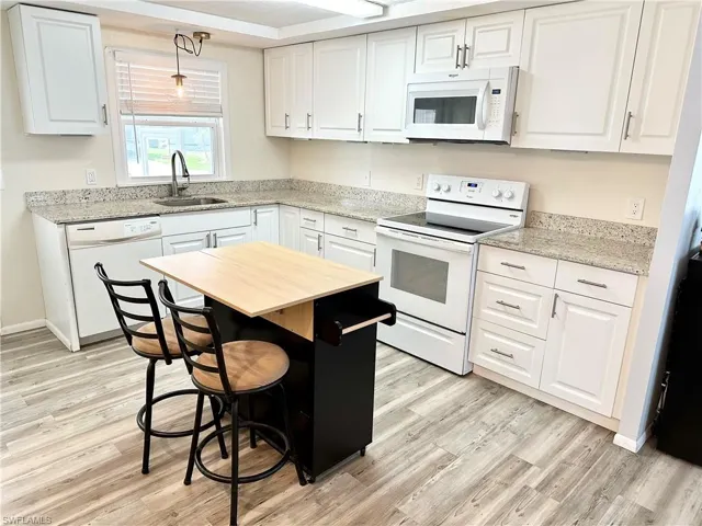 Kitchen with sink, light hardwood / wood-style flooring, white cabinets, and white appliances