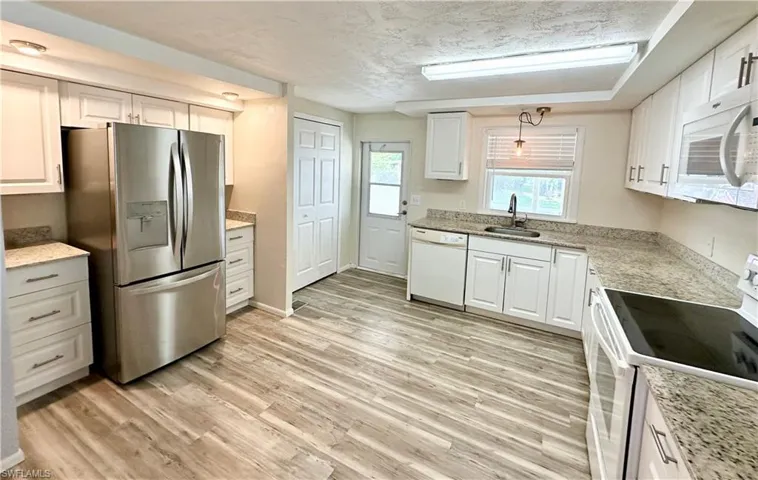 Kitchen featuring hanging light fixtures, light hardwood / wood-style flooring, white appliances, and white cabinetry