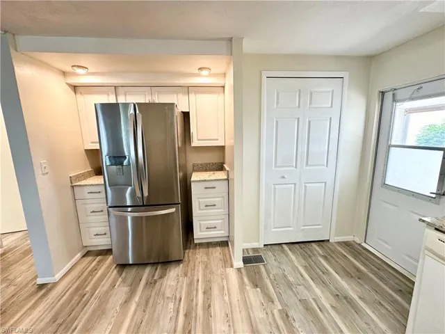 Kitchen featuring stainless steel refrigerator with ice dispenser, hardwood / wood-style floors, light stone countertops, and white cabinets