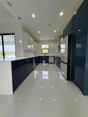 Kitchen featuring light tile patterned floors, white cabinets, hanging light fixtures, and wall chimney range hood