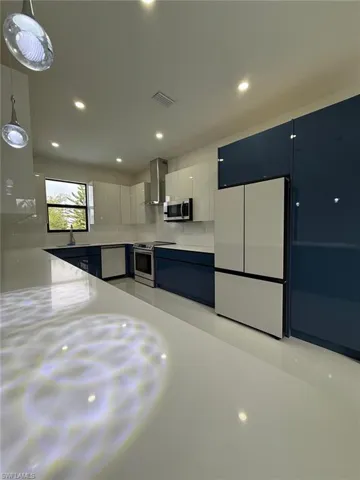 Kitchen featuring sink, hanging light fixtures, appliances with stainless steel finishes, white cabinets, and wall chimney exhaust hood