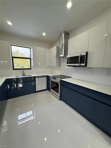 Kitchen featuring sink, white cabinetry, wall chimney range hood, and stainless steel appliances