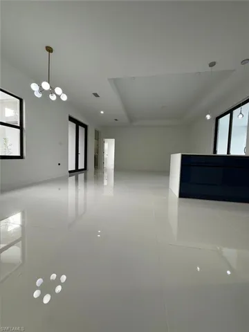 Tiled empty room with a tray ceiling, a healthy amount of sunlight, and an inviting chandelier