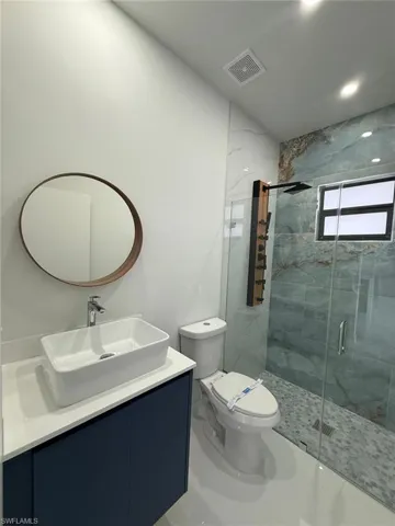 Bathroom featuring a shower with door, toilet, and vanity