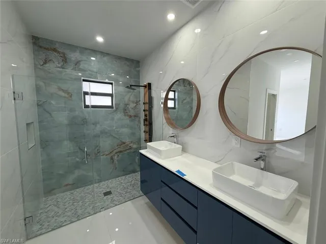 Bathroom featuring a shower with shower door, vanity, and tile walls