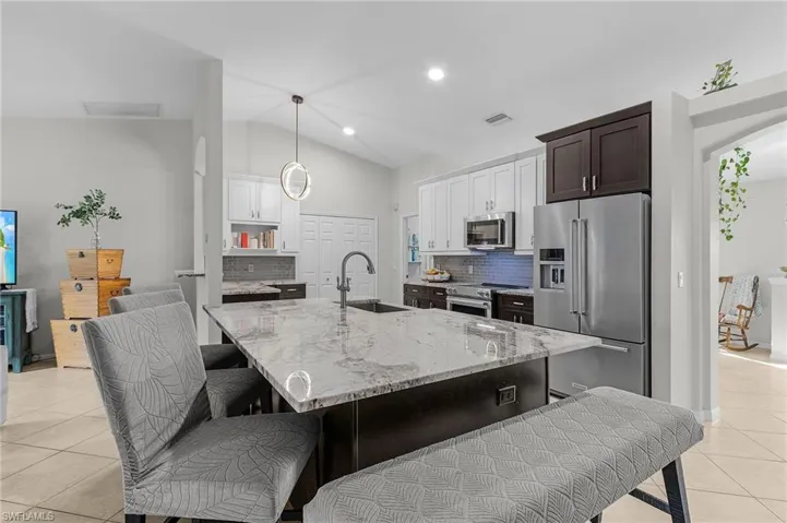 Kitchen featuring light tile patterned floors, arched walkways, light stone counters, appliances with stainless steel finishes, and a sink