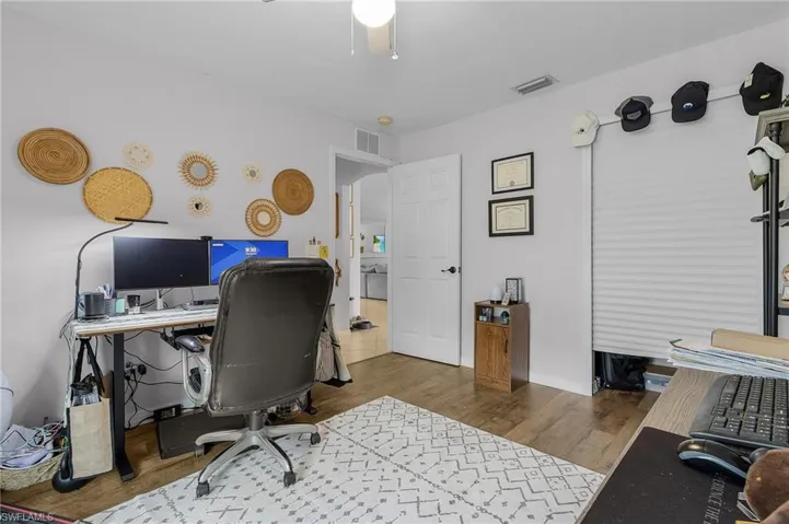 Office area with arched walkways, wood finished floors, visible vents, and baseboards