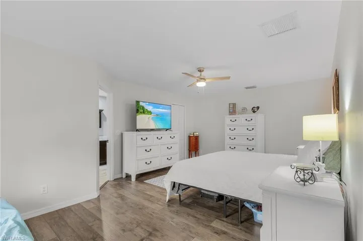 Bedroom with a ceiling fan, wood finished floors, visible vents, and baseboards