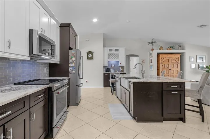 Kitchen featuring arched walkways, appliances with stainless steel finishes, light tile patterned floors, and a breakfast bar