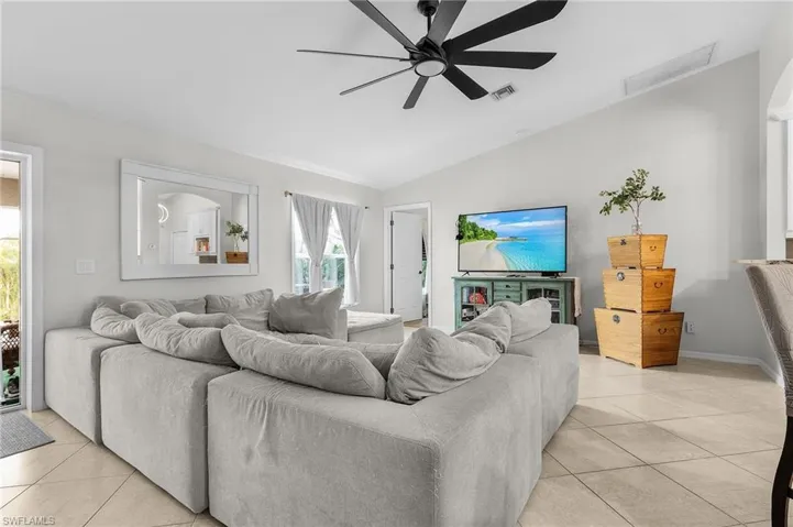 Living room with light tile patterned floors, vaulted ceiling, visible vents, and a ceiling fan