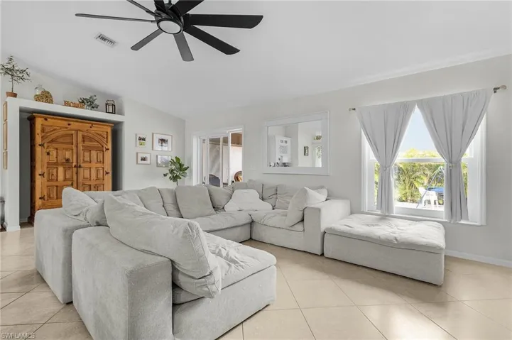 Living area with lofted ceiling, light tile patterned floors, visible vents, and a ceiling fan
