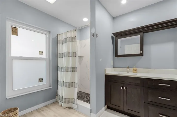 Full bathroom featuring baseboards, a shower with curtain, wood finished floors, vanity, and recessed lighting