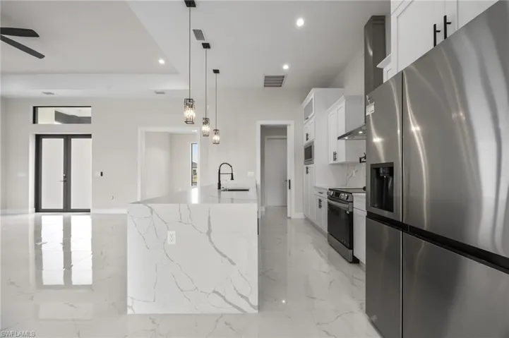 Kitchen featuring stainless steel appliances, white cabinets, light stone countertops, and light marble finish floors