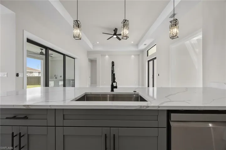 Kitchen featuring light stone countertops, a tray ceiling, stainless steel dishwasher, ceiling fan, and gray cabinets