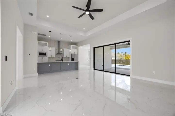 Unfurnished living room featuring a raised ceiling, recessed lighting, ceiling fan, and light marble finish floors