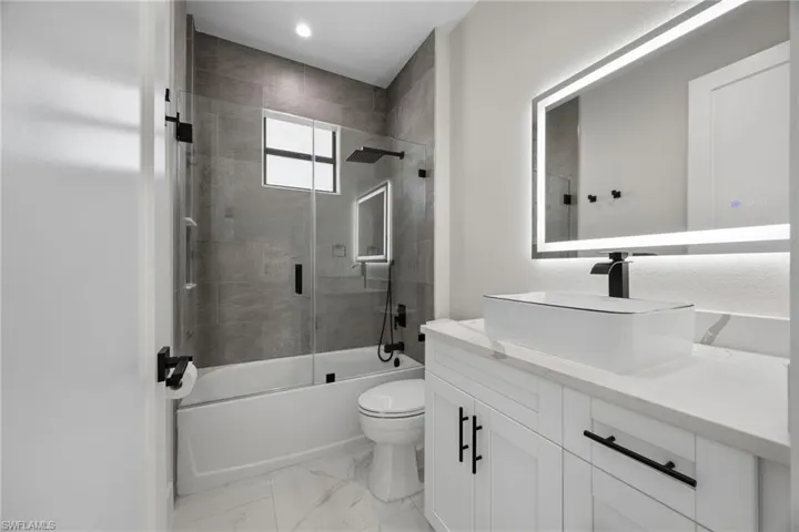 Bathroom featuring vanity, shower / bath combination with glass door, and light marble finish flooring