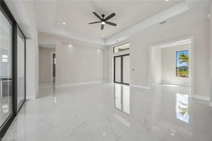 Empty room featuring french doors, a tray ceiling, a ceiling fan, recessed lighting, and light marble finish flooring