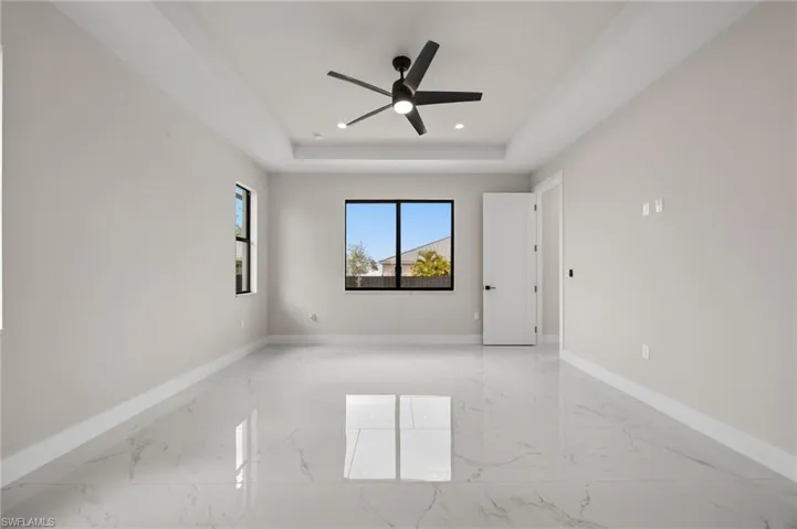 Empty room featuring ceiling fan, light marble finish flooring, a raised ceiling, and recessed lighting