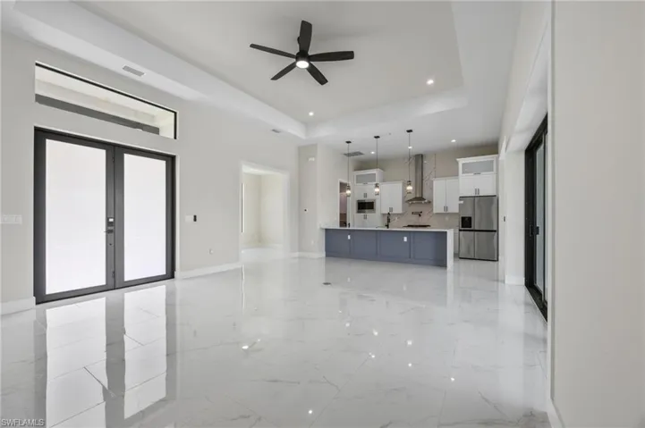 Unfurnished living room featuring ceiling fan, french doors, light marble finish flooring, a tray ceiling, and recessed lighting