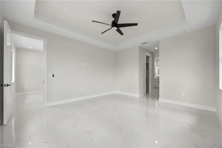 Unfurnished room featuring a tray ceiling, ceiling fan, recessed lighting, and light marble finish floors