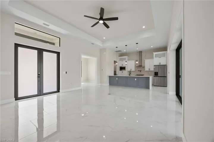 Unfurnished living room with a ceiling fan, a raised ceiling, recessed lighting, french doors, and light marble finish floors