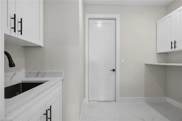 Laundry area featuring cabinet space and light marble finish floors
