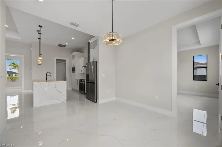 Kitchen with plenty of natural light, a tray ceiling, stainless steel appliances, white cabinetry, and suspended lighting