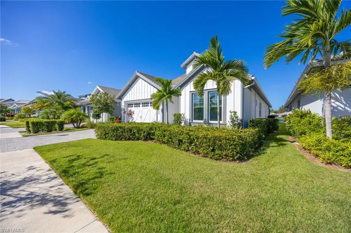 Single-story exterior featuring board-and-batten siding, a multi-pane garage door, a tile roof, mature palm trees, and manicured hedges