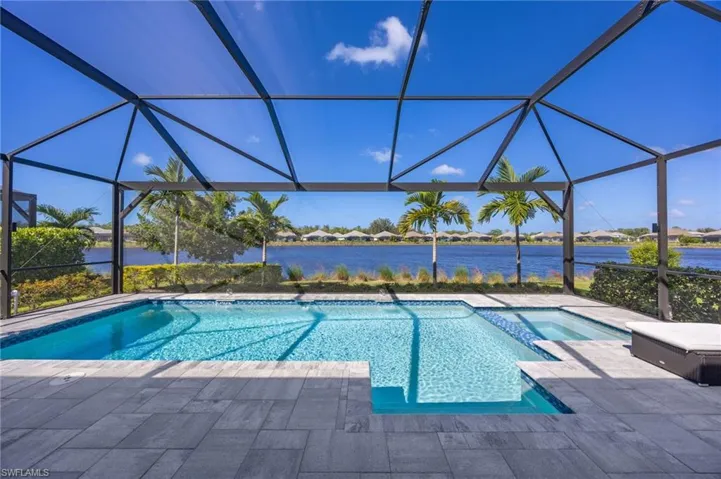Screened-in pool area featuring a built-in spa, stone-finish paver decking, and water-facing orientation