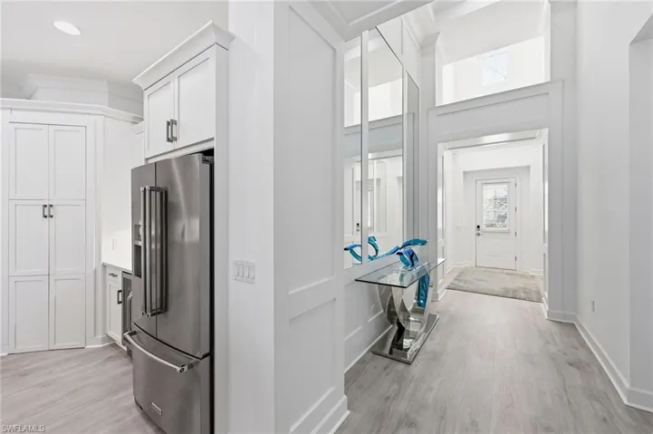 Tall ceilings with transom windows, custom floor-to-ceiling wainscoting, integrated stainless steel appliances, crisp white shaker-style cabinetry, and wood-finish flooring