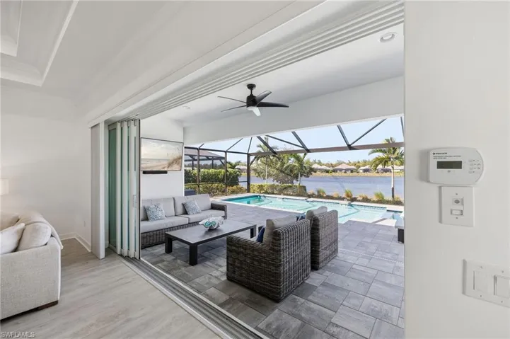 Retractable glass door system, covered patio with stone-finish tile flooring, screened-in pool, ceiling-mounted fan, and waterfront backdrop