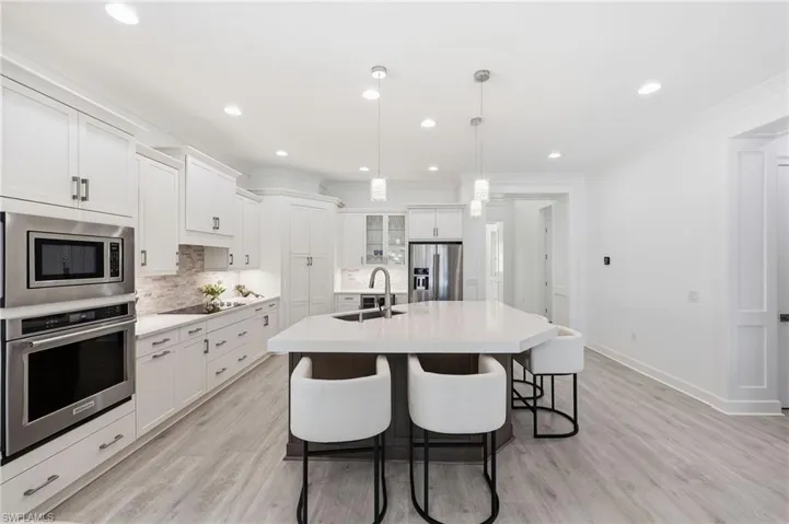 Kitchen featuring white cabinetry, stone-surfaced center island with a built-in sink, stainless steel wall-mounted oven and microwave, recessed lighting, and wood-finish flooring