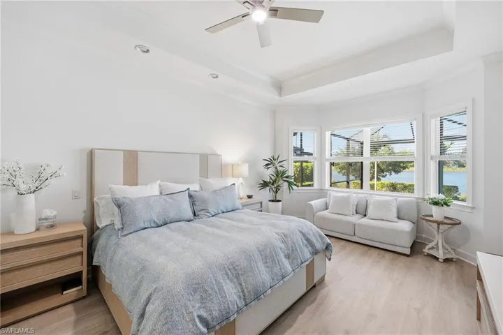 Tray ceiling with recessed lighting, wood-finish flooring, bay windows, and a ceiling fan with integrated lighting