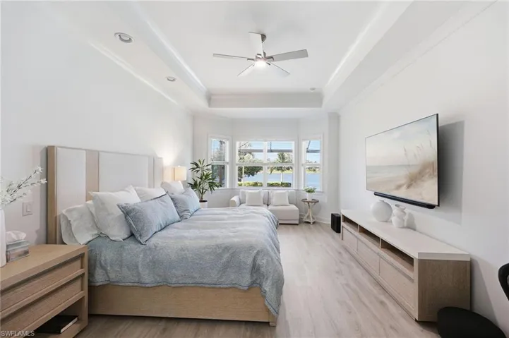 Tray ceiling with integrated recessed lighting, wood-finish flooring, bay window, and ceiling fan