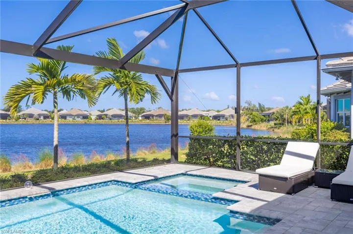Screened lanai featuring a swimming pool, attached spa, stone paver decking, and waterfront backdrop