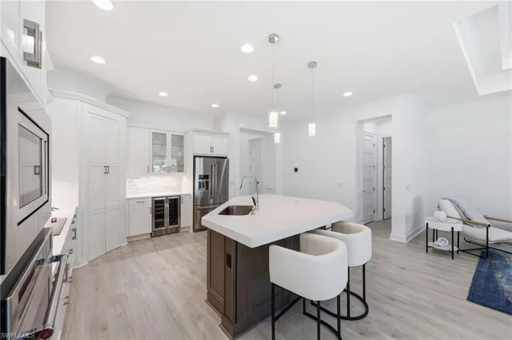 Kitchen featuring white cabinetry, quartz countertops, a multi-sided island with an under-mount sink, integrated stainless steel appliances, and wood-finish flooring