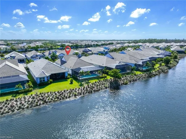 Waterfront property featuring a screened-in swimming pool, paved patio, tiled roof, and expansive lawn