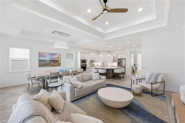 Tray ceiling with integrated recessed lighting, wood-finish flooring, kitchen island with built-in cabinetry, and multi-light pendant fixtures