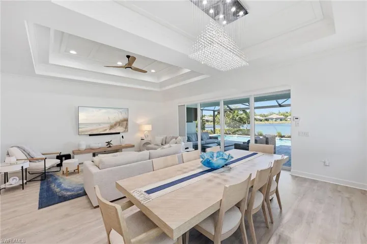 Tray ceiling with recessed lighting, rectangular crystal chandelier, multi-panel sliding glass doors, and light-toned wood-finish flooring